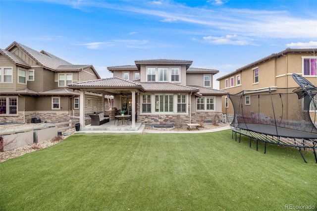 back of house featuring a trampoline, a tile roof, a yard, a patio, and stone siding