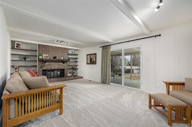 interior space with a brick fireplace, beam ceiling, track lighting, and light colored carpet