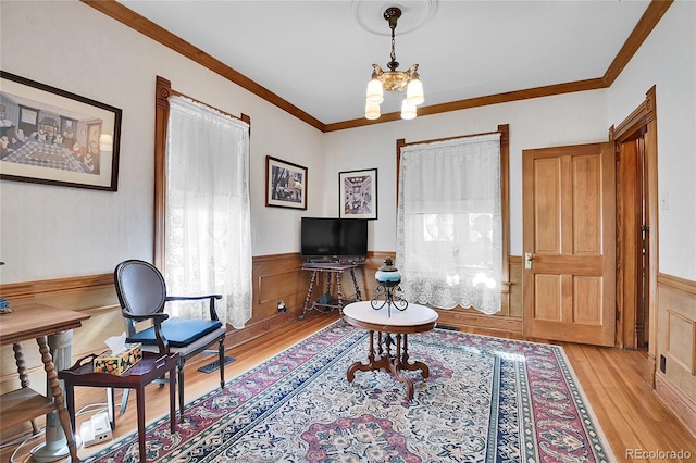 interior space with a wainscoted wall, crown molding, light wood finished floors, and a notable chandelier