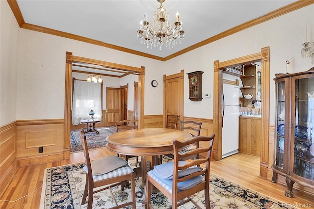 dining area featuring light wood-type flooring, crown molding, a notable chandelier, and wainscoting