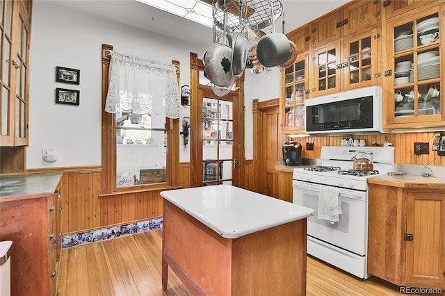 kitchen featuring white appliances, wooden walls, brown cabinets, and a wainscoted wall