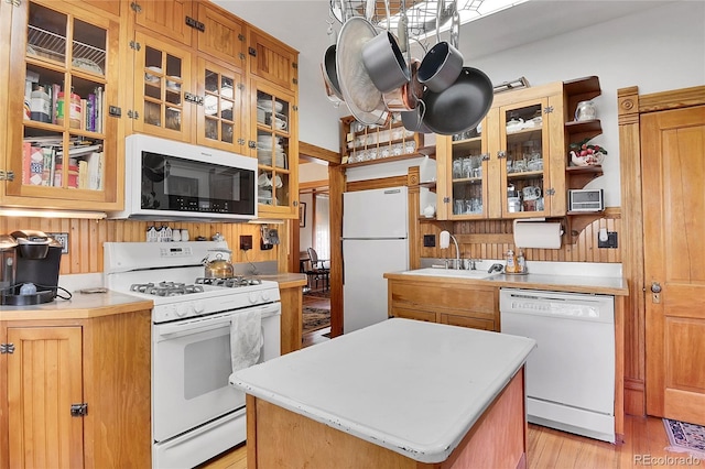 kitchen with light wood finished floors, light countertops, a kitchen island, a sink, and white appliances