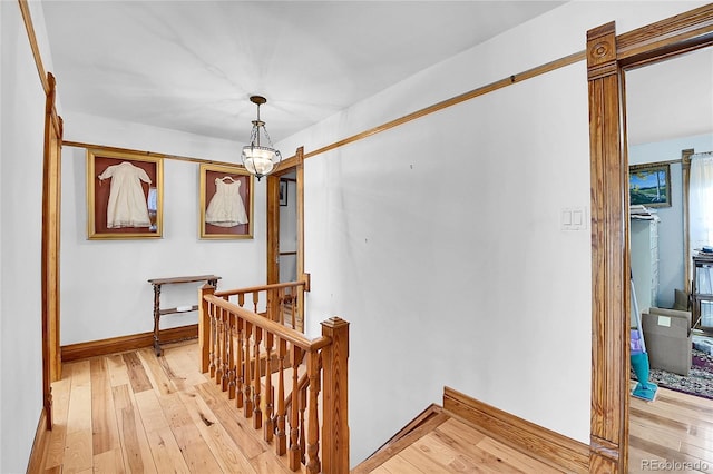 hallway featuring a chandelier, baseboards, light wood finished floors, and an upstairs landing