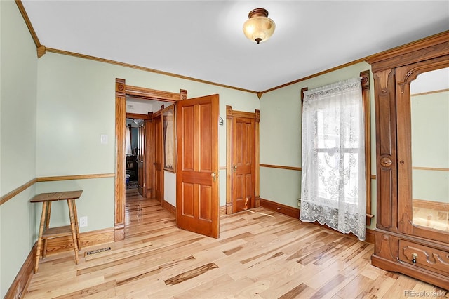 empty room with ornamental molding, light wood finished floors, and baseboards