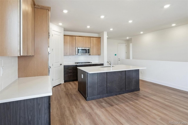 6384 E 154th Pl, Thornton, CO 80602 - kitchen with stainless steel microwave, a sink, a center island with sink, light wood finished floors, and decorative backsplash