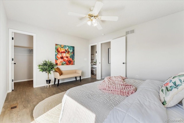 bedroom featuring a spacious closet, baseboards, wood finished floors, and visible vents