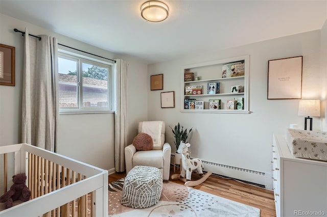 bedroom with a nursery area, baseboard heating, and light hardwood / wood-style flooring