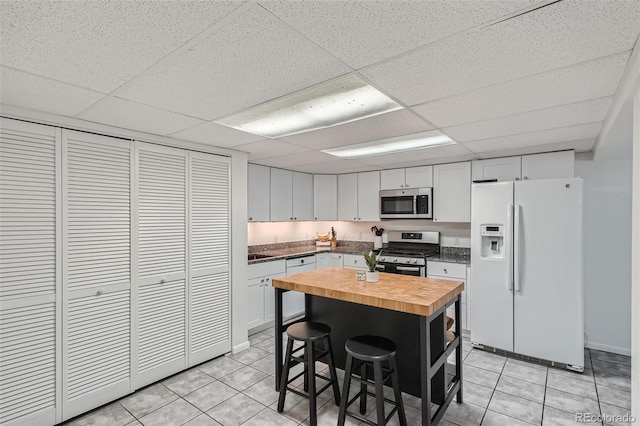 kitchen with butcher block countertops, light tile patterned floors, a breakfast bar area, appliances with stainless steel finishes, and white cabinetry