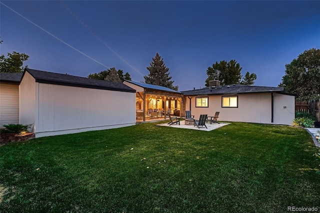 back house at dusk featuring a patio area and a lawn