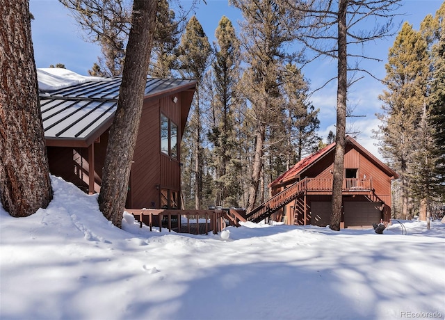 snow covered property featuring stairs, a wooden deck, and a garage