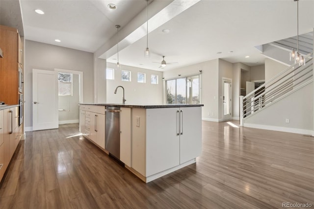 kitchen featuring decorative light fixtures, dark wood-type flooring, stainless steel appliances, and a center island with sink