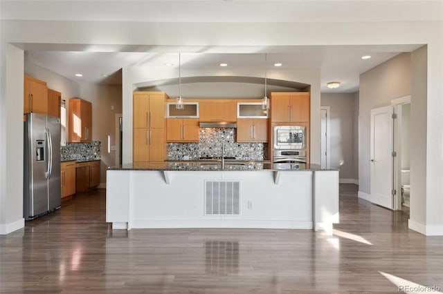 kitchen featuring stainless steel appliances, decorative light fixtures, ventilation hood, and a breakfast bar area