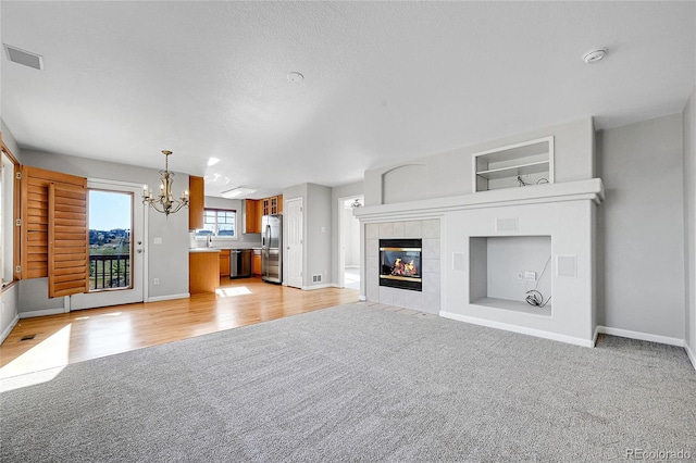 7511 S Sicily Way, Aurora, CO 80016 - unfurnished living room featuring light carpet, a chandelier, baseboards, a tiled fireplace, and light wood-type flooring