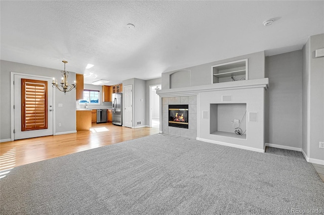 7511 S Sicily Way, Aurora, CO 80016 - unfurnished living room with light colored carpet, a chandelier, baseboards, a tile fireplace, and a textured ceiling