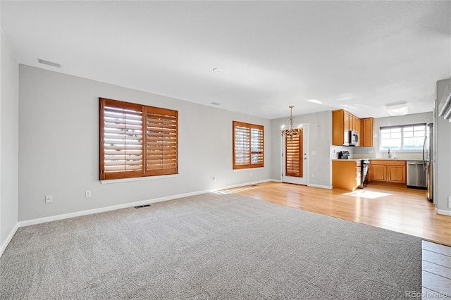 7511 S Sicily Way, Aurora, CO 80016 - unfurnished living room with light carpet, a chandelier, baseboards, and a sink