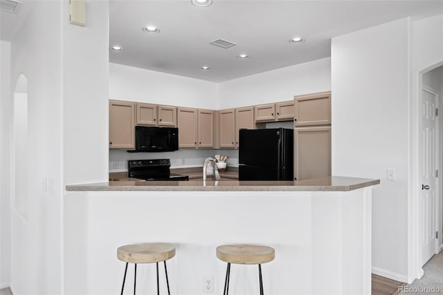 kitchen with a breakfast bar, black appliances, light brown cabinetry, and kitchen peninsula