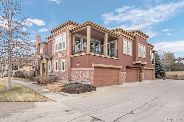 view of side of property with an attached garage, a balcony, driveway, stucco siding, and a chimney