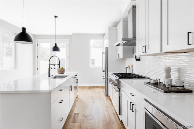 1541 Glencoe St, Denver, CO 80220 - kitchen with wall chimney range hood, a sink, stainless steel appliances, light wood-style floors, and white cabinetry