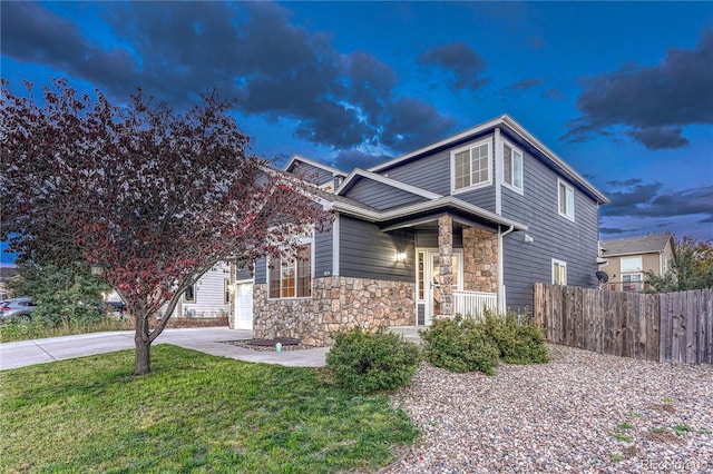 view of front of property featuring a front lawn, stone siding, fence, concrete driveway, and a garage