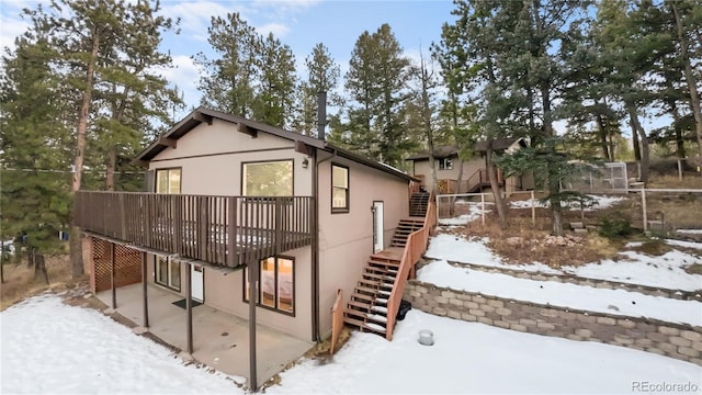 view of snow covered exterior featuring a deck, stucco siding, stairs, and a patio