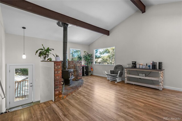 living area with a wood stove, wood finished floors, beamed ceiling, and baseboards