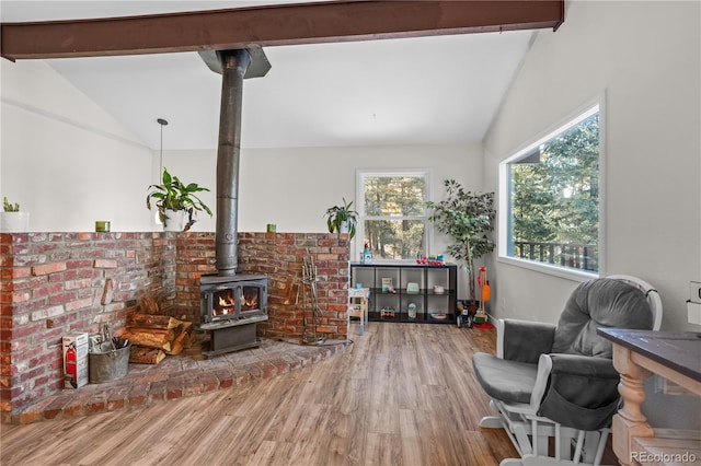 living area featuring a wood stove, vaulted ceiling with beams, and wood finished floors