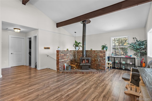 living area with a wood stove, wood finished floors, and vaulted ceiling with beams