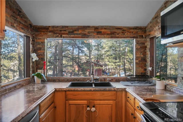 kitchen featuring brown cabinets, appliances with stainless steel finishes, lofted ceiling, and a sink