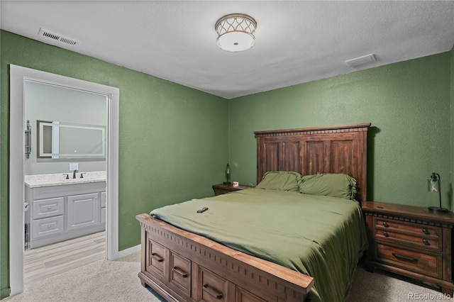 bedroom featuring light carpet, a textured wall, visible vents, and connected bathroom