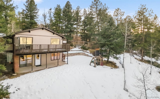 snow covered property with stucco siding, a wooden deck, and a patio