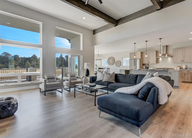 living room featuring beam ceiling, light wood-type flooring, a notable chandelier, and sink