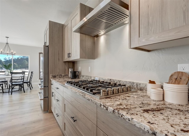 kitchen featuring light brown cabinetry, appliances with stainless steel finishes, pendant lighting, and wall chimney range hood