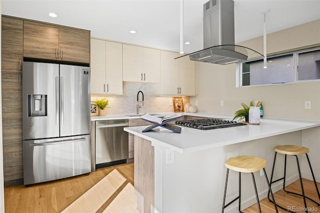 kitchen with stainless steel appliances, island exhaust hood, kitchen peninsula, light hardwood / wood-style floors, and a breakfast bar area