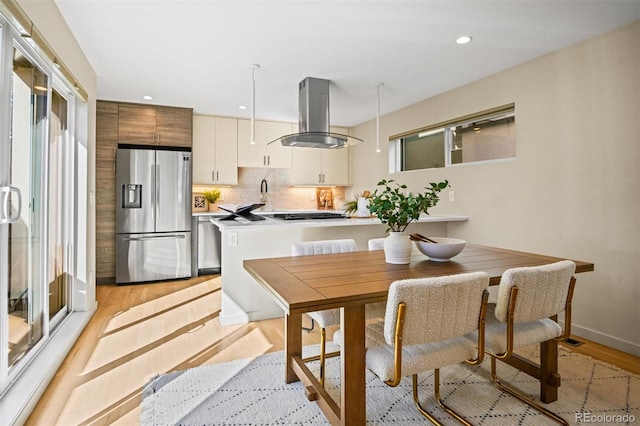 kitchen with backsplash, island range hood, stainless steel appliances, and light hardwood / wood-style floors