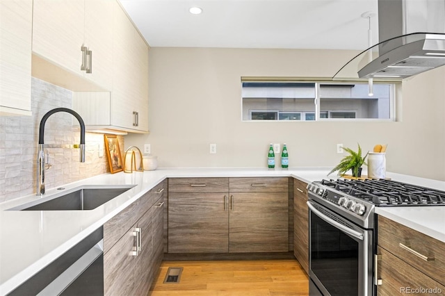 kitchen featuring decorative backsplash, appliances with stainless steel finishes, island range hood, sink, and light hardwood / wood-style flooring