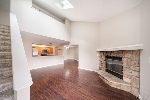 unfurnished living room with a stone fireplace, a skylight, dark hardwood / wood-style floors, and a towering ceiling