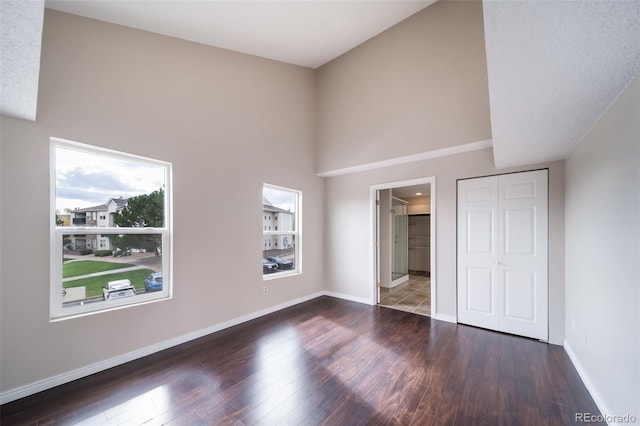 unfurnished bedroom featuring connected bathroom, a towering ceiling, dark wood-type flooring, and a closet