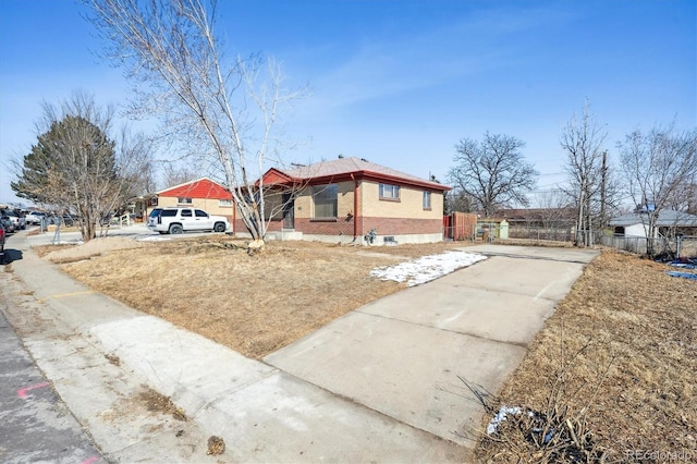 view of front facade with driveway, fence, and brick siding