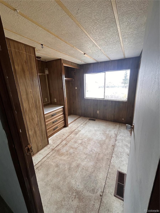 unfurnished bedroom featuring wooden walls, a closet, and a textured ceiling