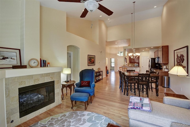 living room with light wood-style flooring, a high ceiling, ceiling fan with notable chandelier, a fireplace, and recessed lighting