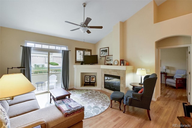 living room with arched walkways, high vaulted ceiling, a fireplace, a ceiling fan, and light wood-style floors