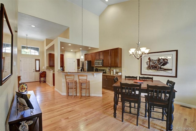 dining space with an inviting chandelier, baseboards, light wood finished floors, and high vaulted ceiling