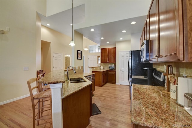 kitchen featuring light wood-style flooring, stainless steel microwave, a high ceiling, a kitchen bar, and a sink