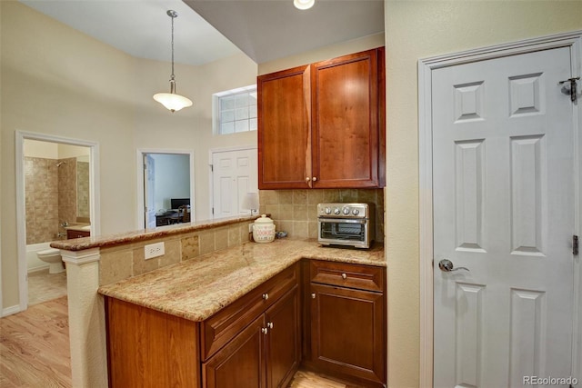 kitchen with decorative backsplash, a peninsula, light stone countertops, hanging light fixtures, and light wood-style floors