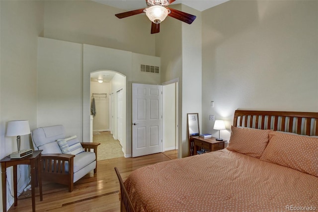 bedroom featuring arched walkways, a towering ceiling, baseboards, visible vents, and light wood-style floors