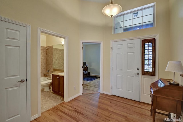 foyer entrance featuring baseboards, a towering ceiling, and light wood finished floors