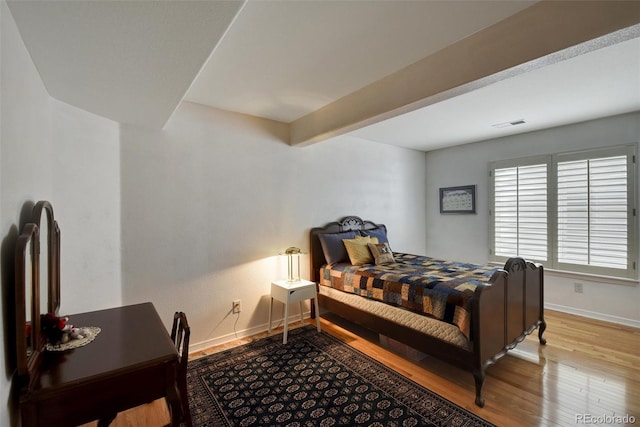 bedroom featuring beam ceiling, visible vents, baseboards, and wood finished floors