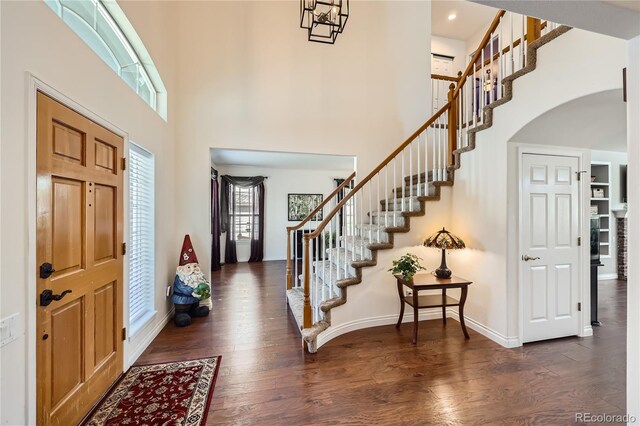 foyer entrance featuring arched walkways, a towering ceiling, wood finished floors, baseboards, and stairs