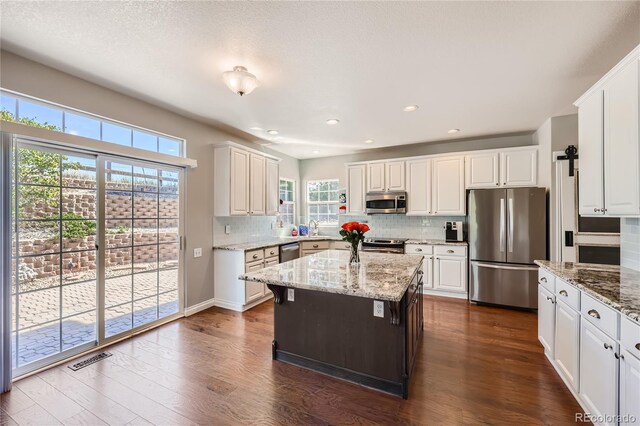 kitchen with stainless steel appliances, visible vents, white cabinets, backsplash, and dark wood finished floors