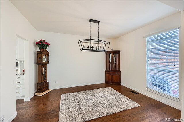 unfurnished dining area featuring an inviting chandelier, baseboards, visible vents, and dark wood-type flooring